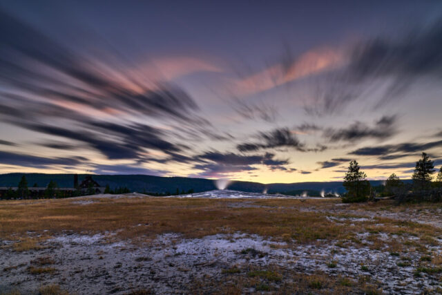 Long exposure image of Old Faithful geyser in Yellowstone National Park taken during blue hour, with steam rising in low light
