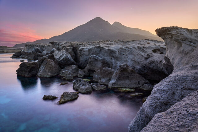 Landscape photograph of Los Escullos cliffs in Almería, Spain at sunset showing volcanic mountains and coastline in warm light