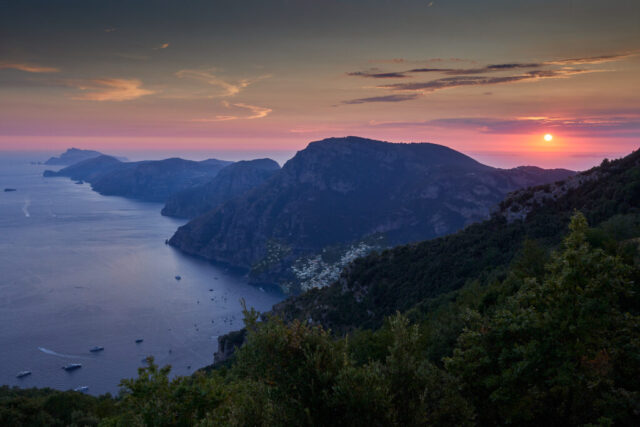 Landscape photograph of the Amalfi Coast at sunset showing Positano in the foreground and Capri in the background seen from a viewpoint